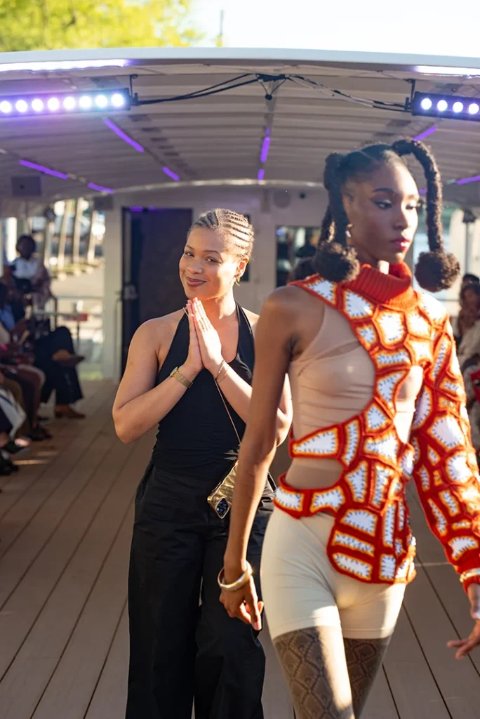 Mannequin qui défile avec la pièce Karo, avec derrière elle la créatrice Cynthia Eugénie